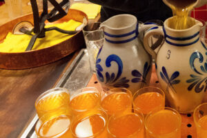 Apfelwein wird in einen traditionellen Adolf-Wagner-Bembel gegossen, daneben mehrere gefüllte Gläser auf einem Kupfertablett